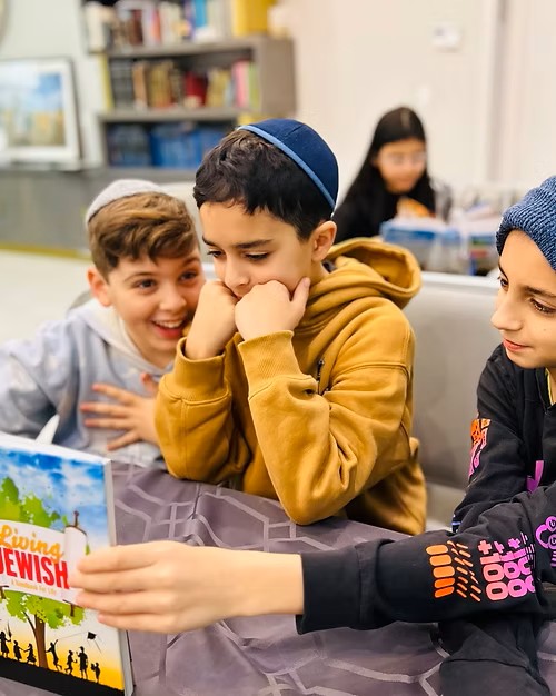 Kids wearing kippahs reading a Jewish education book together at Hebrew school