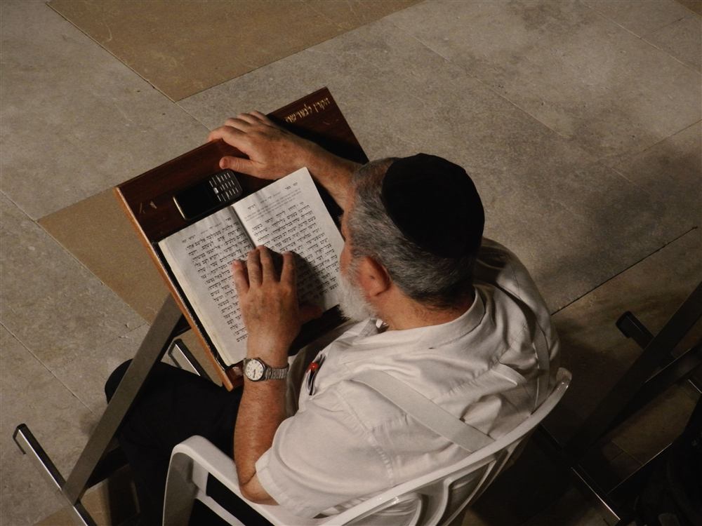 A man wrapped in a tallit reading from a siddur during prayer services